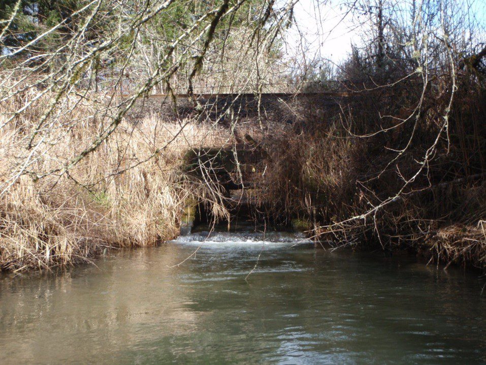 Railroad trestle with water flowing underneath before dropping down a small waterfall.